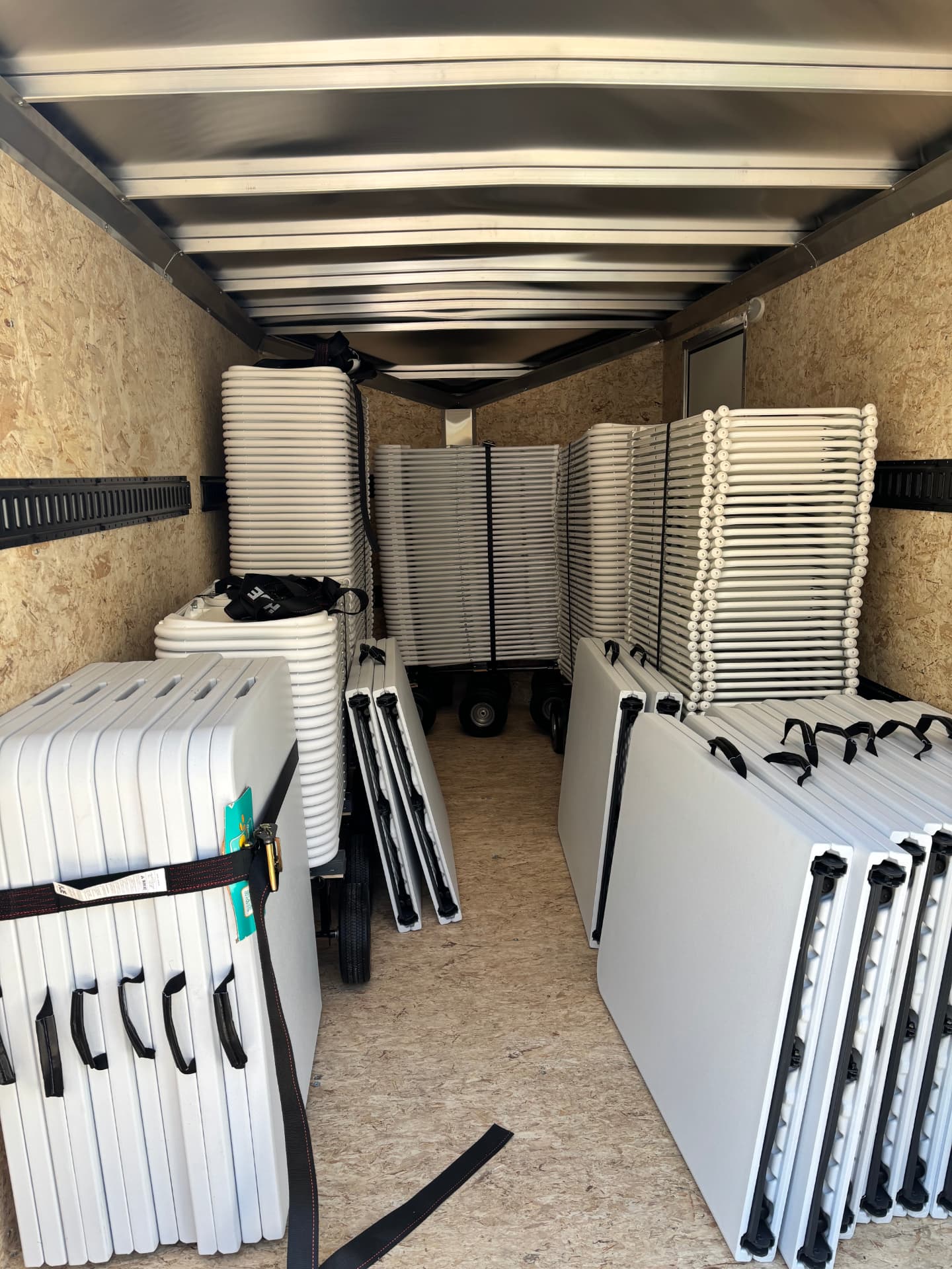 Stacks of white folding chairs and folded tables loaded and ready for delivery