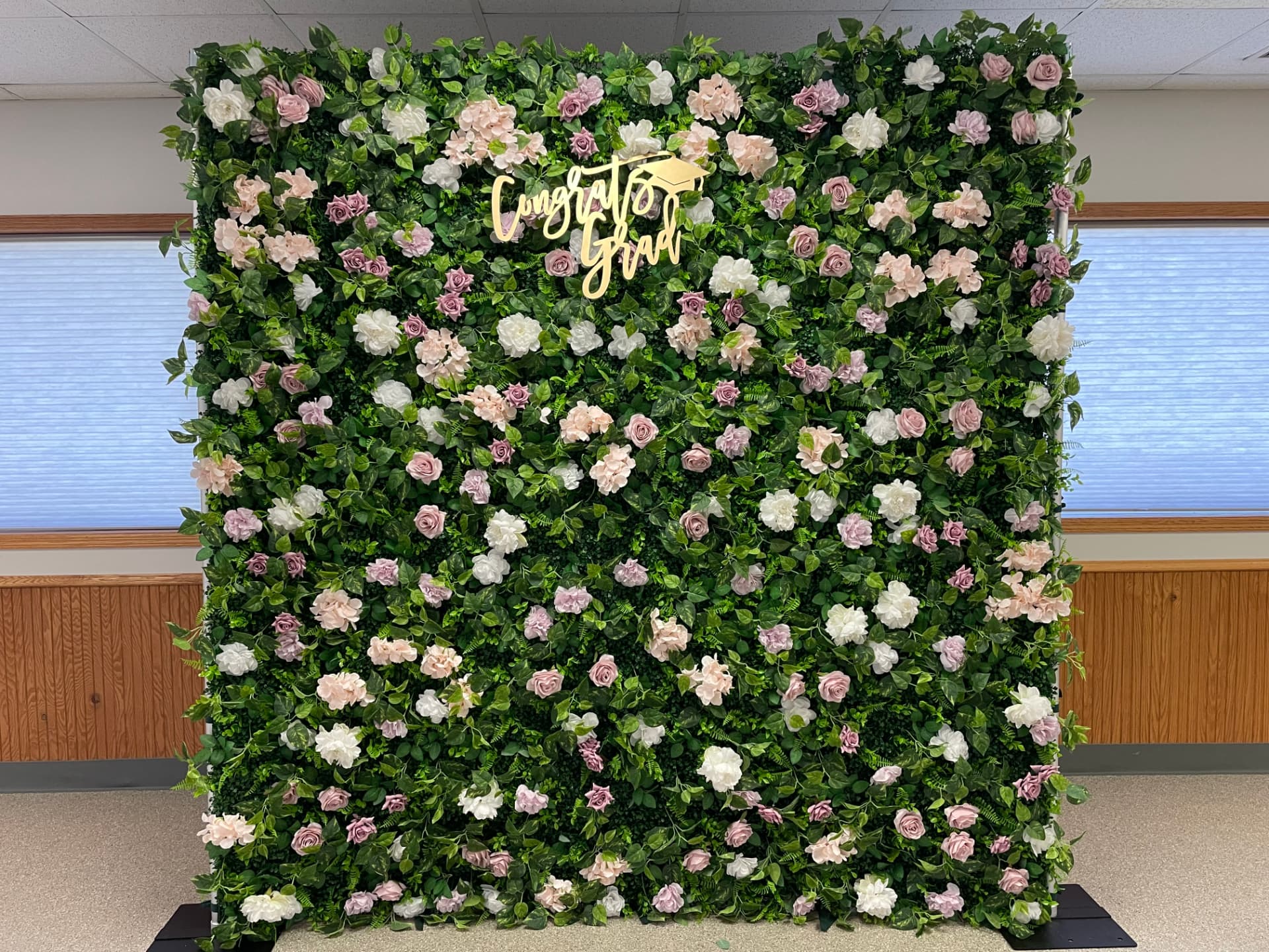 Greenery and flower wall backdrop with a gold Congrats Grad sign at a graduation celebration