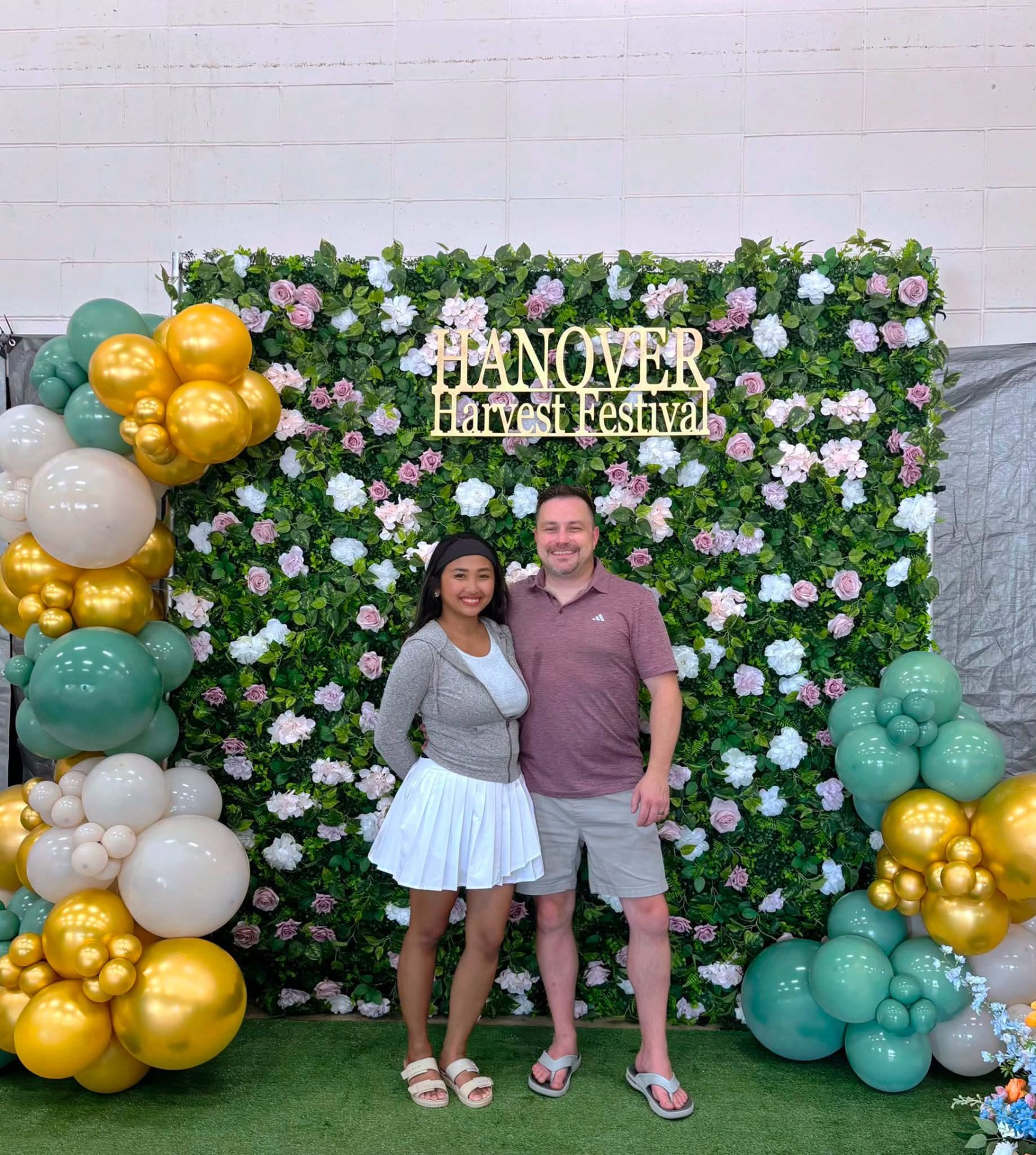 Guests posing in front of a greenery and flower wall framed by gold and sage balloon accents at the Hanover Harvest Festival