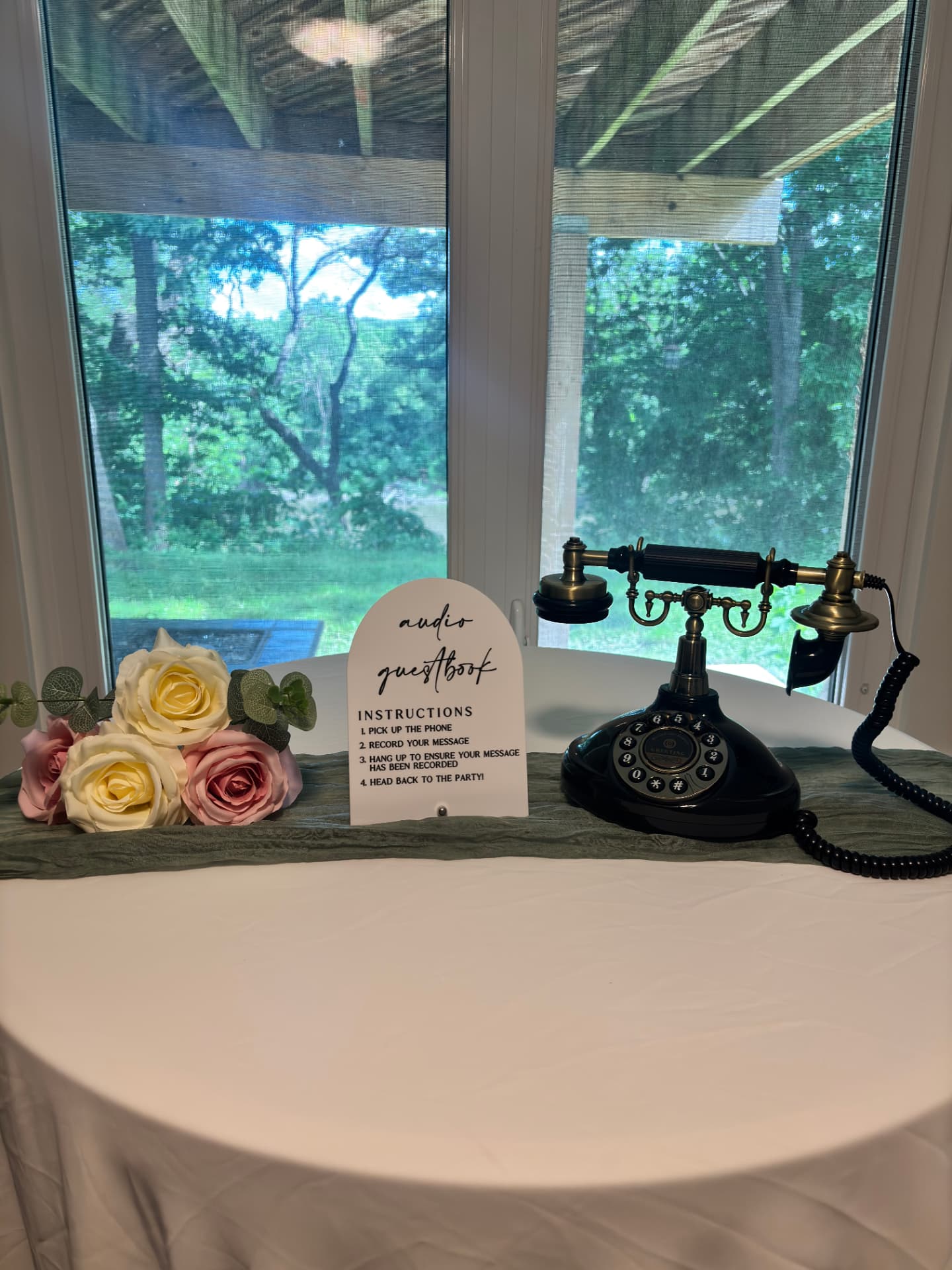 Vintage black and brass rotary audio guest book phone beside an instructions sign and dusty pink roses