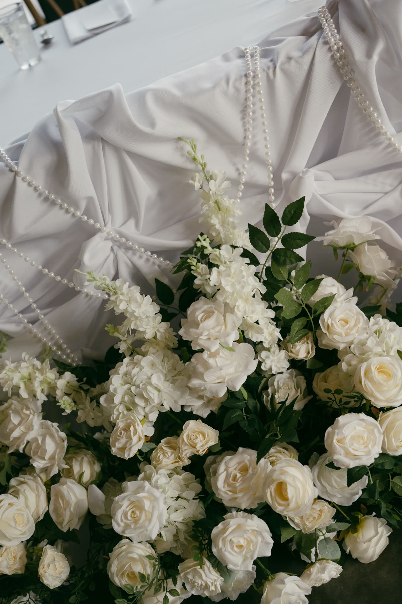 White roses, hydrangeas, and greenery styled along a draped white head table at a luxury wedding